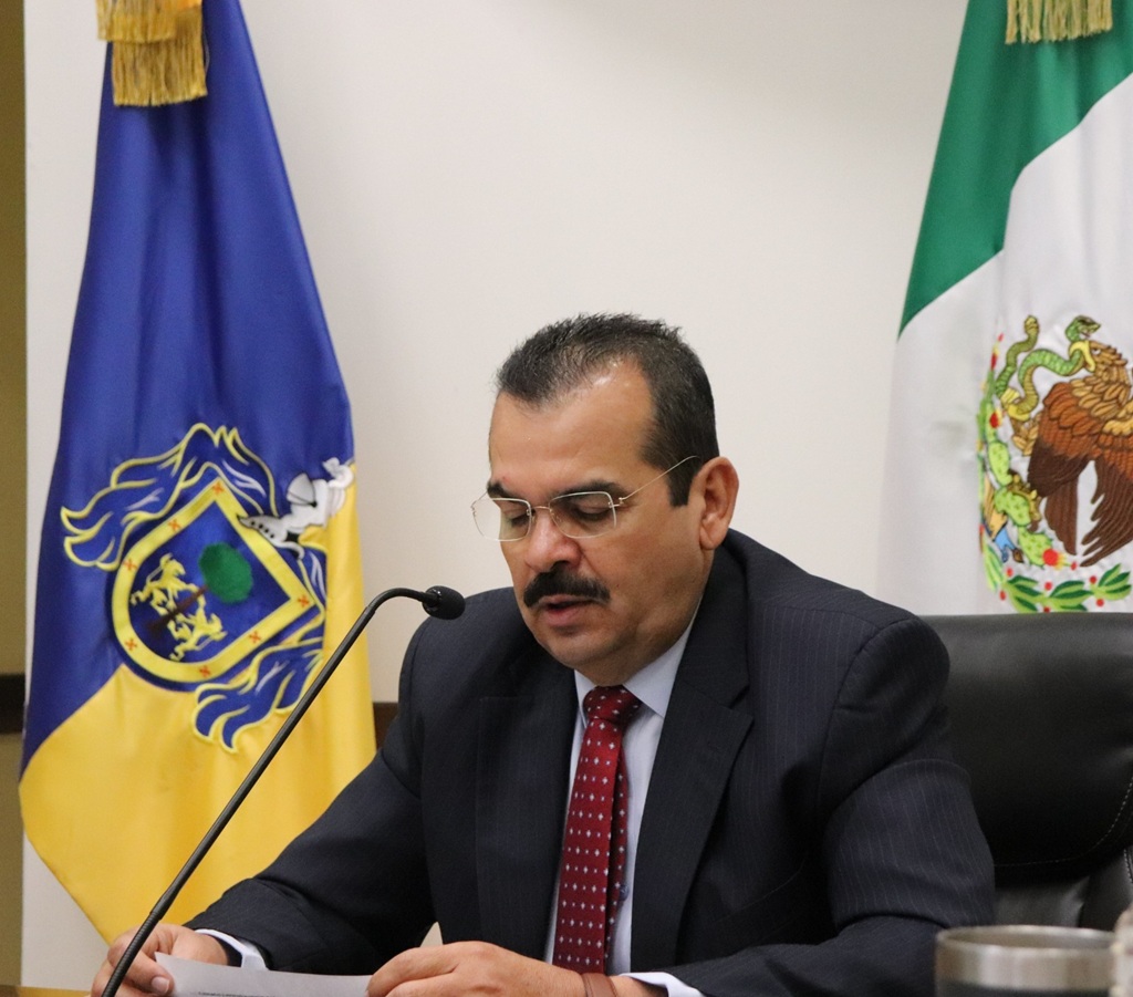 un hombre con bigote, sentado leyendo frente a un micrófono