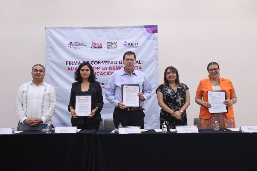 Personas participantes parados en el estrado mostrando el convenio firmado.