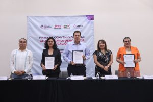 Personas participantes parados en el estrado mostrando el convenio firmado.