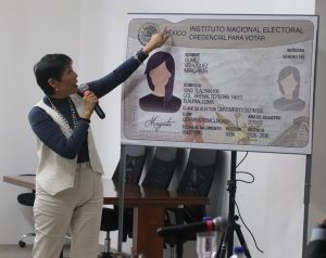persona de pie cabello corto señalando una imagen gigante de la credencial para votar del INE
