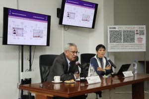 dos personas sentadas, uno habla habla frente a un micrófono