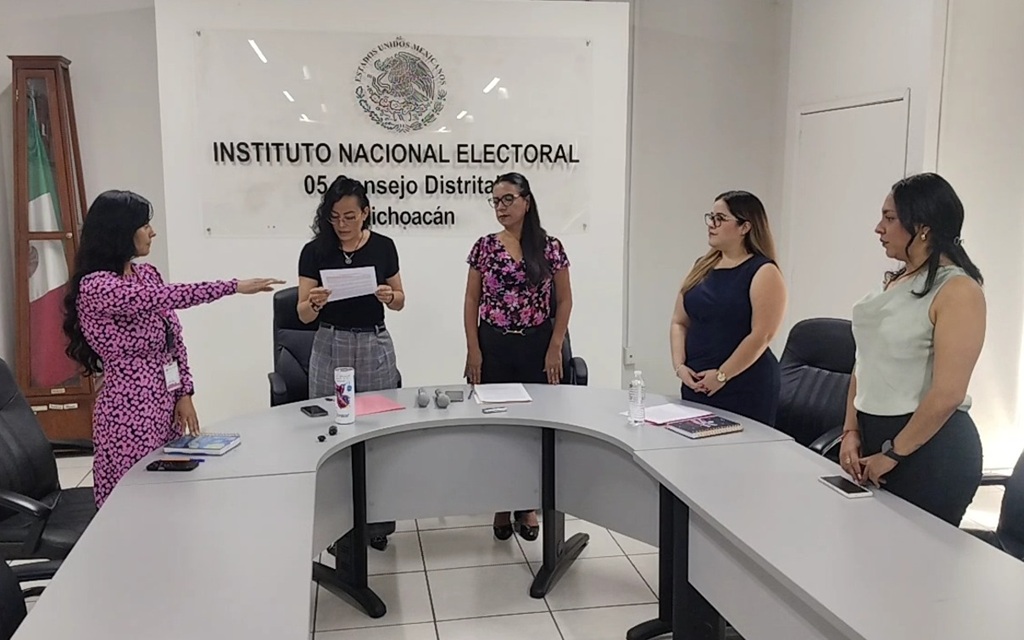 cinco mujeres de pie, una de ellas con el brazo extendido al frente