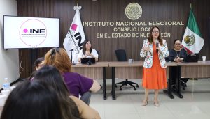 una mujer de pie vestido rojo saco blanco hablando por micrófono