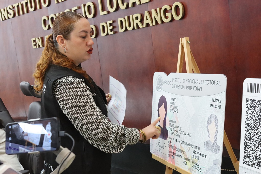 una mujer pelo rojizo señalando una credencial tamaño cartulina