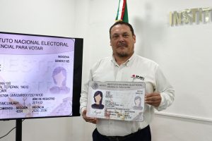 un hombre de pie sosteniendo un ejemplar de credencial tamaño cartulina