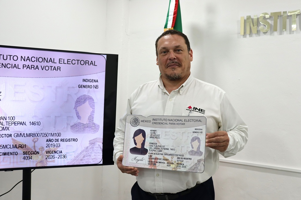 un hombre de pie sosteniendo un ejemplar de credencial tamaño cartulina