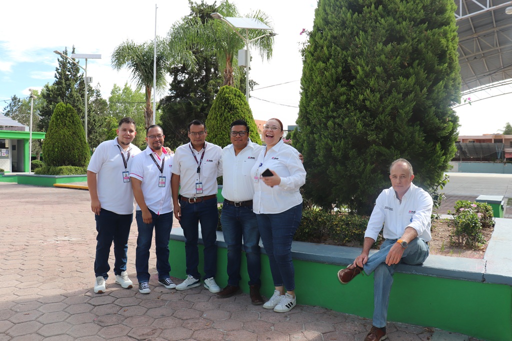 seis personas de pie en una jardinera, todos visten pantalón de mezclilla azul y camisa blanca
