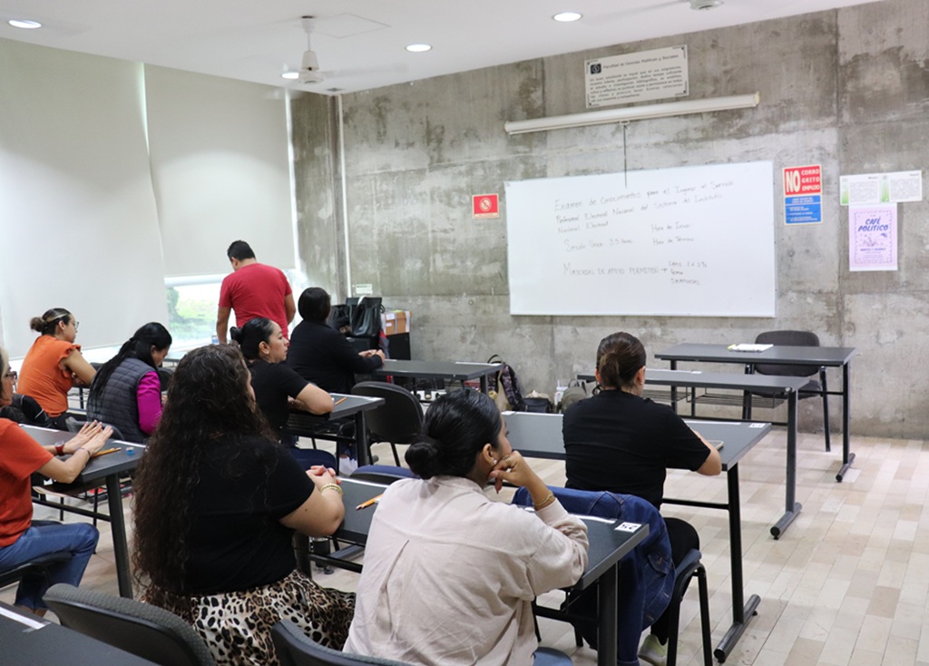 personas sentadas en un salón de clases frente a un pizarrón blanco