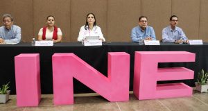 dos mujeres y tres hombres frente a una mesa negra y tres letras rosas