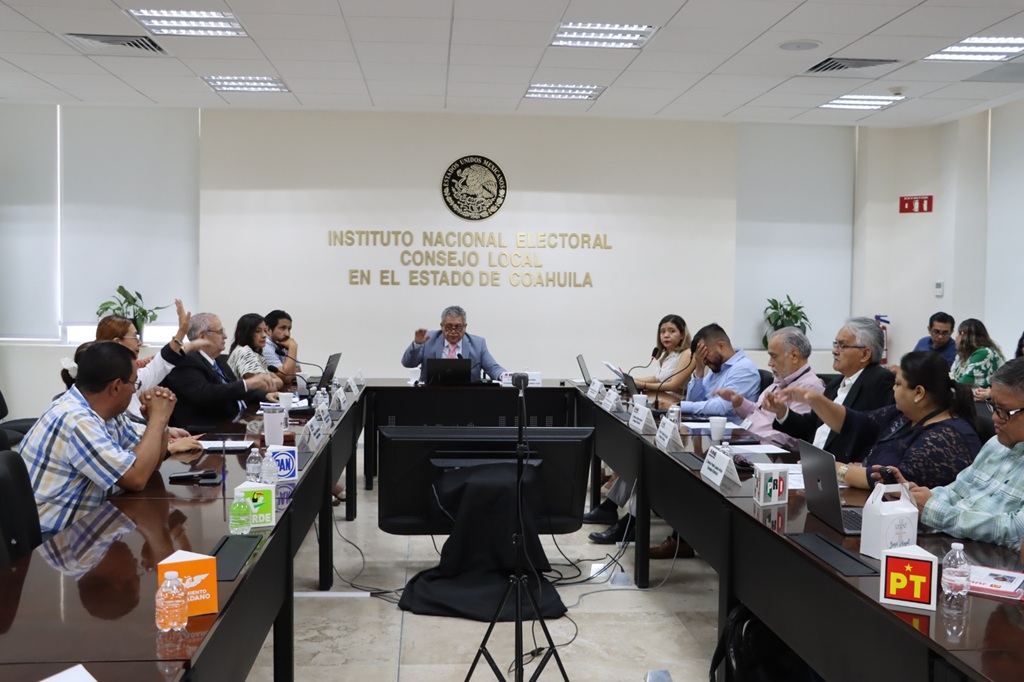 varias personas sentadas en un salón votando a mano alzada