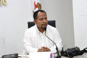 un hombre con camisa blanca sentado frente a un micrófono