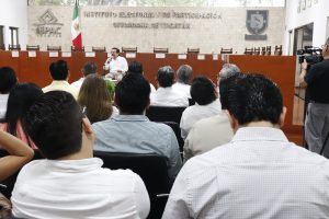 Personas participantes frente a público asistente sentados en el salón.
