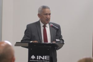 Un hombre cabello cano de pie hablando frente a un micrófono