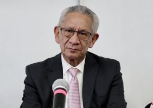 adulto mayor con lentes sentado frente a un micrófono