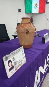 Una bandera de México, una mesa con mantel morado, un jarrón de barro y una credencial para votar
