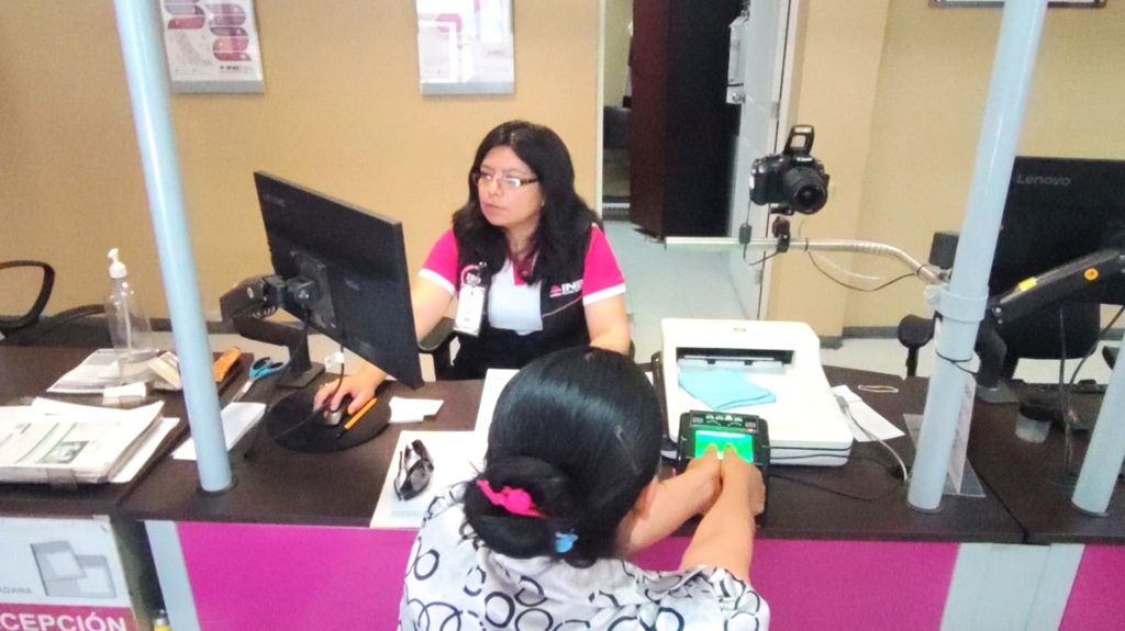 una mujer sentada frente a una computadora, atendiendo a otra mujer