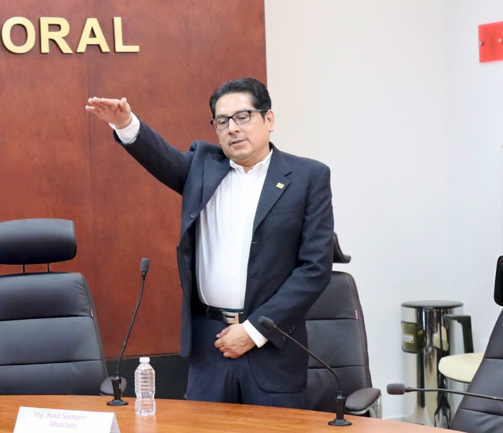 un hombre de saco y pantalón negro, camisa blanca de pie con el brazo derecho extendido al frente