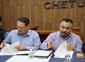 dos hombres sentados firmando documentos