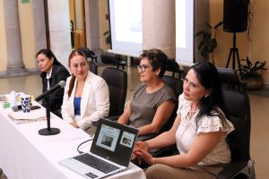 cuatro mujeres sentadas frente a una mesa con micrófonos