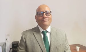 Hombre de lentes, calvo con saco y corbata verde y camisa blanca