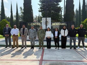 varias personas entre ellos militares de pie frente a un letrero del Ejercito Mexicano