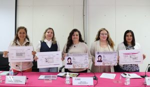 cinco mujeres de pie sosteniendo una credencial tamaño cartulina
