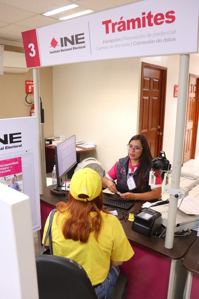 una mujer con gorra y camisa color amarillo sentada tramitando su credencial