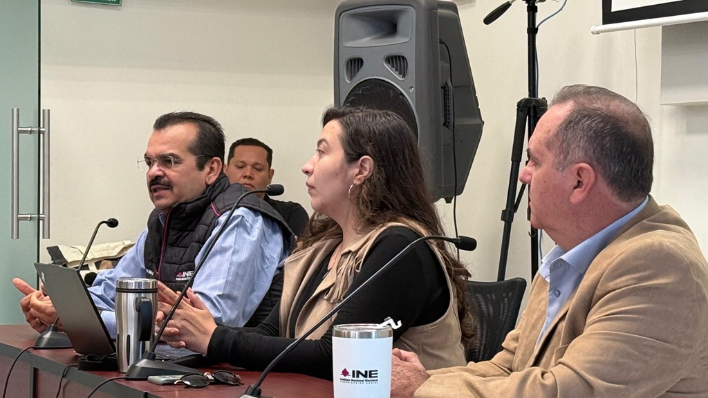 una mujer y dos hombres sentados frente a micrófonos delgados