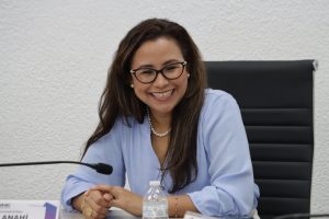 mujer con lentes cabello rizado sentada con una gran sonrisa