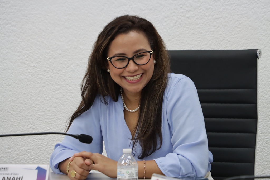 mujer con lentes cabello rizado sentada con una gran sonrisa