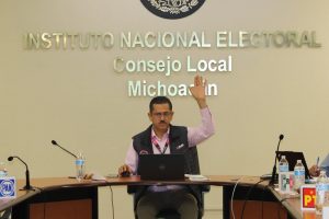 un hombre sentado con lentes votando a mano alzada