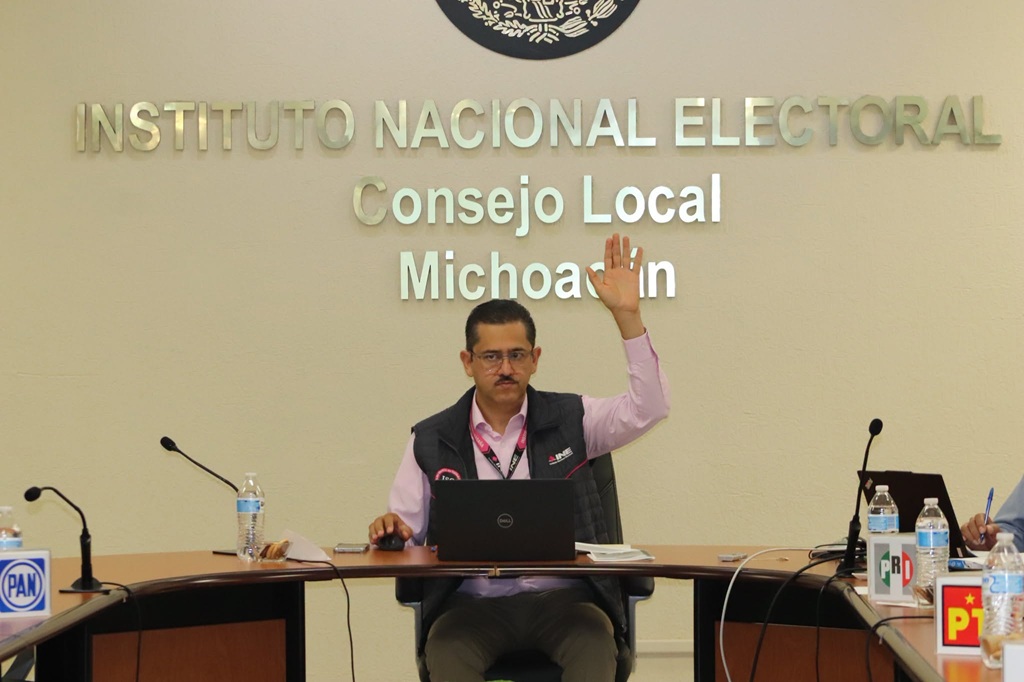un hombre sentado con lentes votando a mano alzada