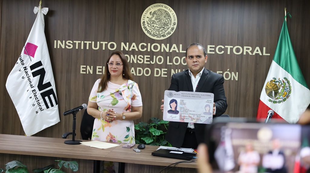 dos personas de pie mostrando un modelo de credencia para votar