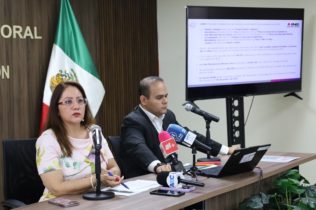 una mujer y un hombres entados frente a varios micrófonos de medios
