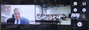 Un señor en una pantalla y a un lado otra pantalla con muchas personas