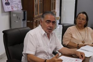 hombre con camisa blanca, sentado a lado de otra mujer que lo mira