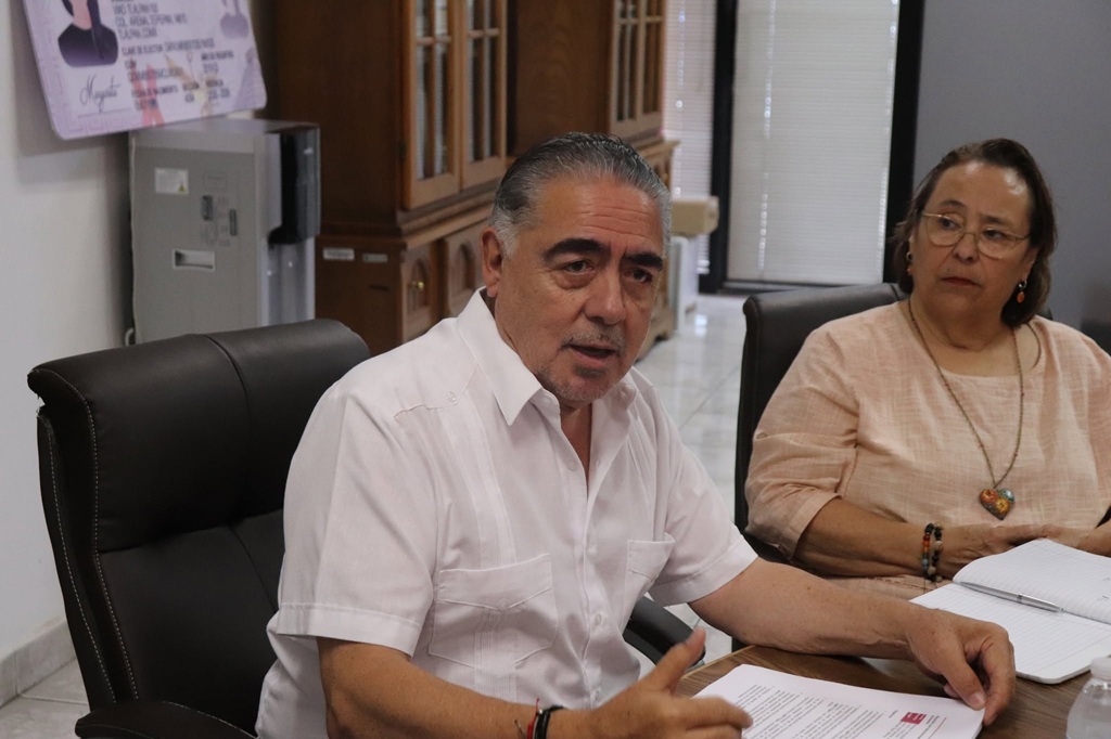 hombre con camisa blanca, sentado a lado de otra mujer que lo mira