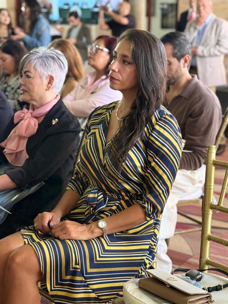 una mujer sentada trae vestido de rayas diagonales, el cabello largo lacio peinado de lado.