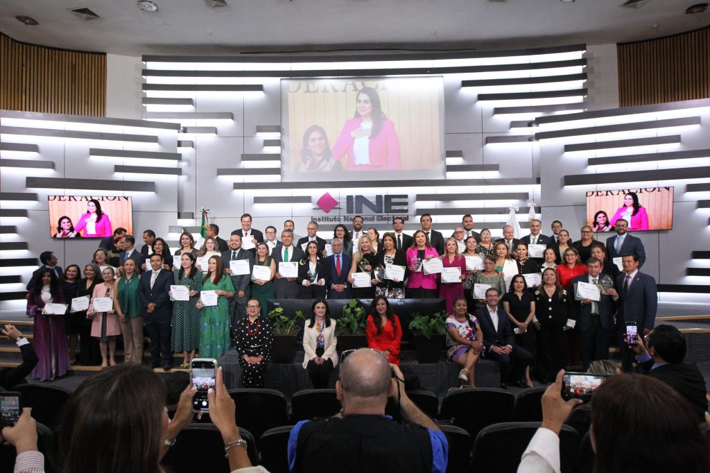 Grupo de personas con diplomas al frente del auditorio del INE