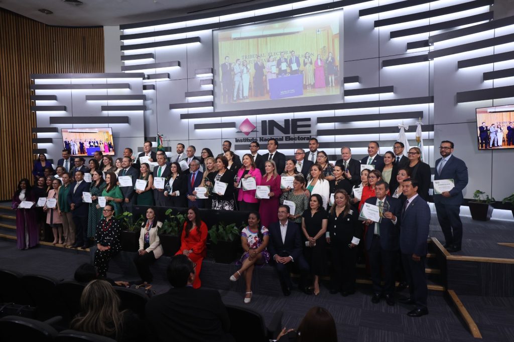 Grupo de personas con diplomas al frente del auditorio del INE