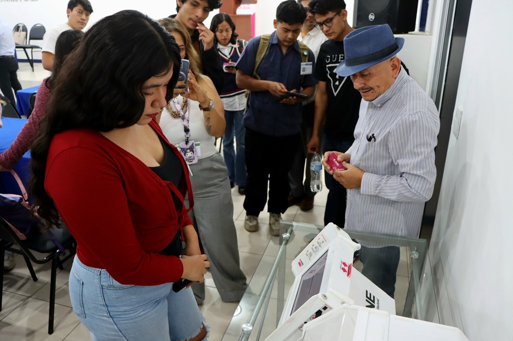 alumnas y alumnos viendo una maquina de votación electrónica