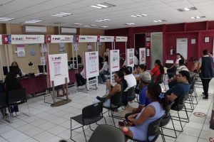 personas sentadas al interior de un módulo del INE esperando ser atendidas