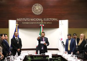 seis personas de pie, en medio un hombre con el brazo derecho extendido al frente