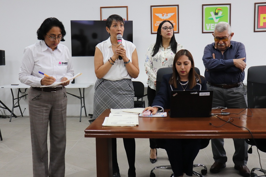 cuatro mujeres y un hombre de pie, una de ella habla mediante micrófono
