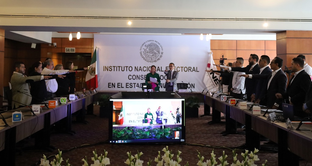 varias personas de pie en un salón, con el brazo derecho extendido hacia enfrente