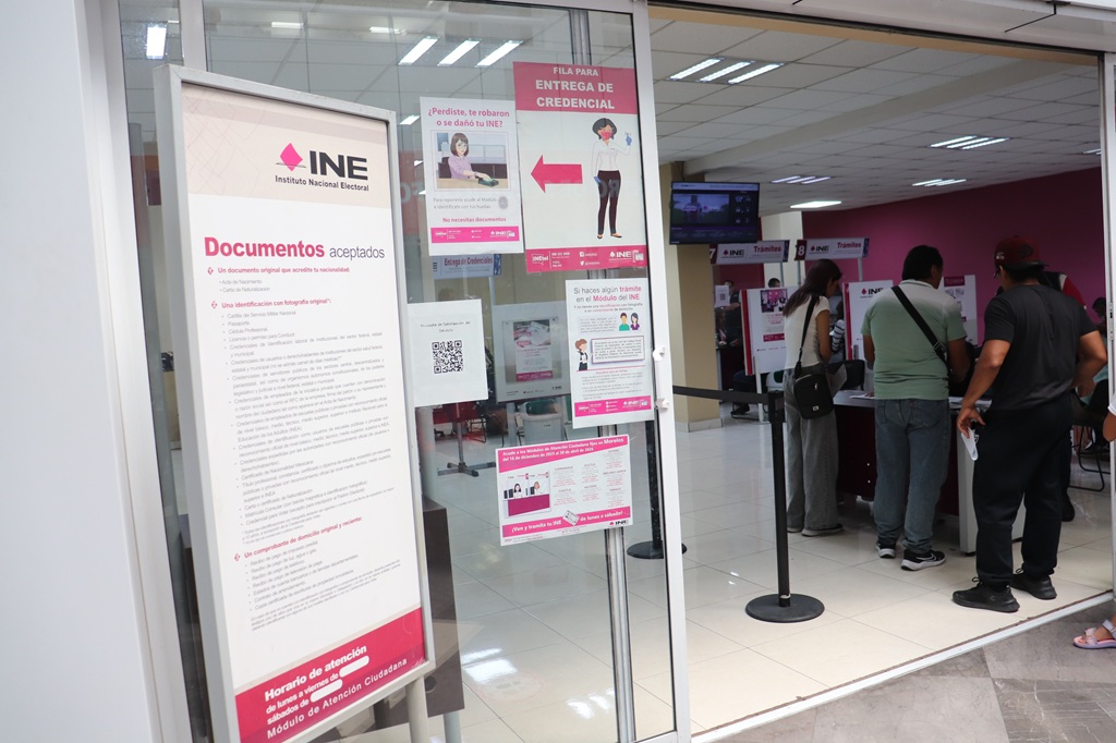 entrada de una oficina, tiene perta de cristal, y letreros color blanco y rosa con letras negras que dicen INE