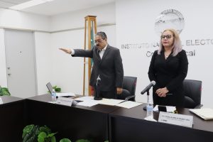 un hombre de pie con el brazo entendido al frente, a su lado una mujer cabello rubio