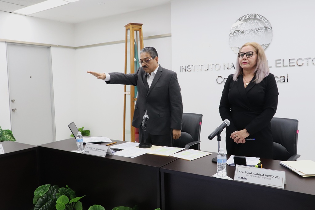un hombre de pie con el brazo entendido al frente, a su lado una mujer cabello rubio