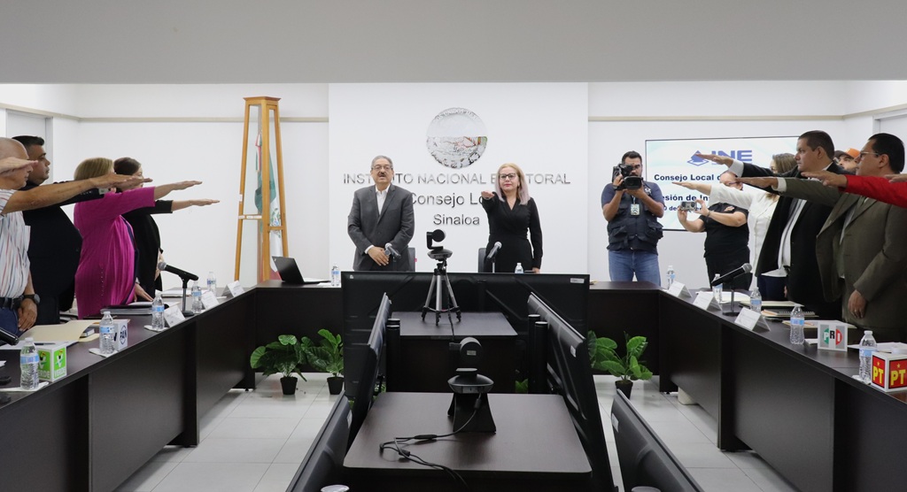 varias personas alrededor de una mesa rectangular con el brazo derecho extendido al frente
