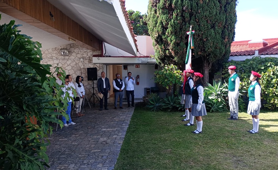 cinco estudiantes uniformadas de pie en línea horizontal sosteniendo la bandera nacional